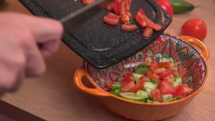 Slow motion hand scraping sliced fresh tomatoes from black cutting board into colorful orange bowl healthy salad preparation home kitchen cooking