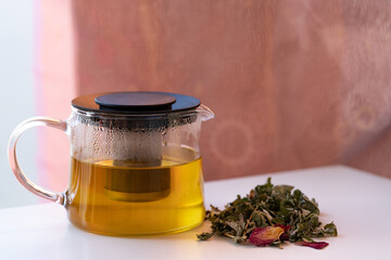 Transparent glass teapot brews golden herbal infusion beside loose leaves; steam and condensation sparkle in soft focus, evoking cozy wellness ritual, natural tea moments and lifestyle.