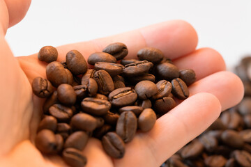 Hand cradles roasted coffee beans in soft light; selective focus highlights texture and aroma, suggesting morning ritual, barista craft and natural coffee lifestyle stories.