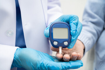 Asian doctor using digital glucose meter for check sample blood sugar level to treatment diabetes.