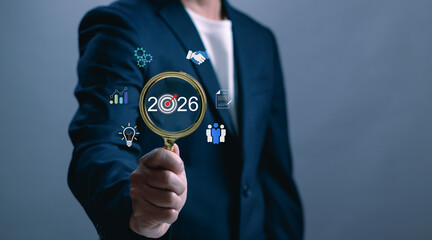 Businessman holding magnifying glass focusing on year 2026 with infographic icons. Concept of business vision, strategic planning, innovation, data analysis and future goals