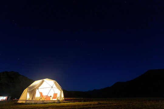 Illuminated camping tent under starry night sky in remote mountain landscape