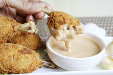 Take one piece of fried chicken and dip it in the bowl of thick salad dressing, then place several pieces of chicken close together on a white plate.

