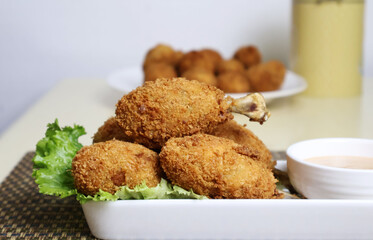 Minced chicken coated in batter and deep-fried, wrapped around the bone, revealing it, arranged on a plate with a thick salad dressing on the same plate.