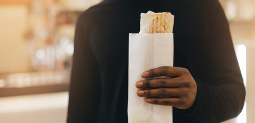 African male adult holding wrapped shawarma sandwich in cafe setting