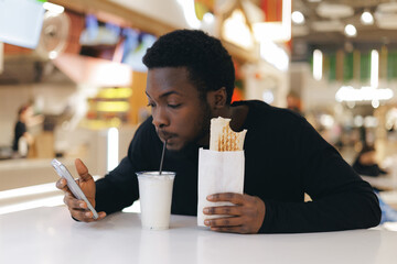 Young african male enjoying snack and drink in modern food court