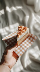Hand holding a cake slice on patterned napkin, inviting mood, soft shadows