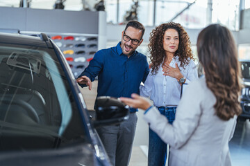 Happy Couple Consults With Salesperson About Car Purchase in Bright Modern Showroom