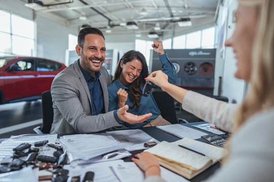 Happy Couple Receives Car Keys From Friendly Dealer At Car Showroom