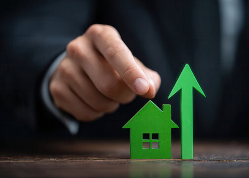 Increase in real estate value represented by a green house model and upward arrow during a business meeting