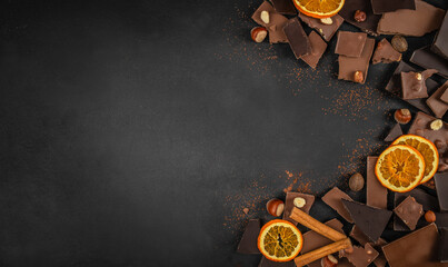 Assorted chocolate pieces with dried orange slices, nuts and cinnamon on dark background with copy...