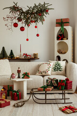 Warm holiday living room with a decorative overhead branch, red ornaments, gifts, and festive accents around a cozy sofa.