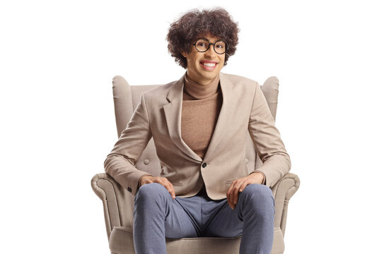 Young man with curly hair and glasses sitting in an armchair