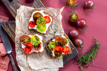 Bruschetta with cream cheese, cherry tomatoes on toasted bread on red background top view