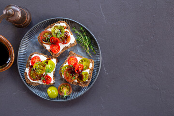 Bruschetta with cream cheese, cherry tomatoes on toasted bread in a plate on dark background top view copy space for text