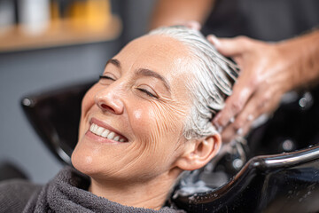A woman enjoys a relaxing hair treatment at a salon, smiling as her hair is washed, highlighting self-care and beauty.