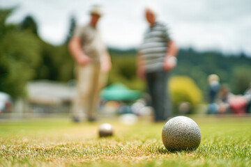 A focused image of a lawn bowling game, showcasing a close-up of a bowling ball on grass with blurred players in the background.