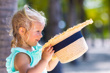 adorable caucasian baby girl in straw hat smiling on sandy beach at hot summer day. Child having...