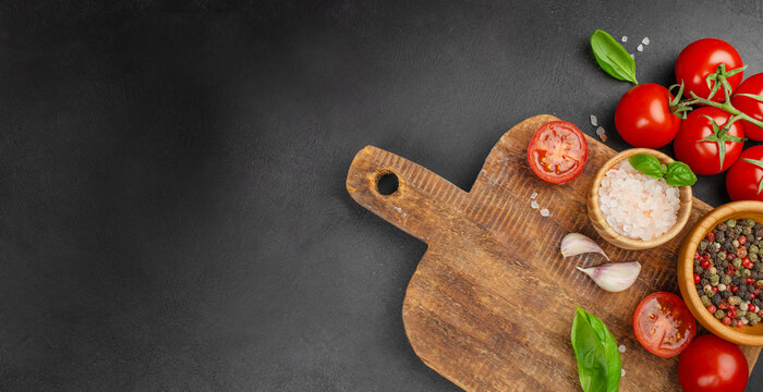 Rustic wooden cutting board with fresh tomatoes, basil, garlic and spices arranged on dark stone background, top view with wide copy space for recipe text, menu design or cooking concepts - Powered by Adobe