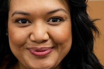 Mid adult woman posing with smooth skin wearing rose lipstick under studio tan backdrop lighting