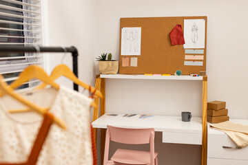 Cork board is displaying fashion sketches, fabric swatches and red fabric sample in design studio