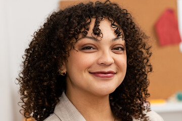 African American woman in blazer smiling at camera in office by corkboard with red fabric, pushpin
