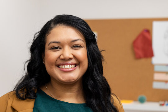 Woman standing in office wearing blazer holding stress ball by cork board with pinned red cloth