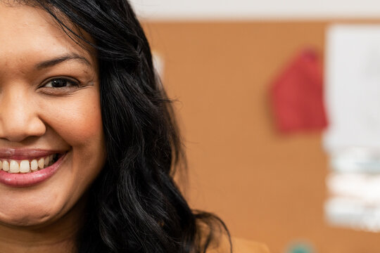 Woman smiling wearing mustard blazer reviewing pinned papers on corkboard in office, copy space