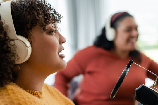 African American women cohosts speaking into pop-filter mics with headphones in studio, copy space - Powered by Adobe