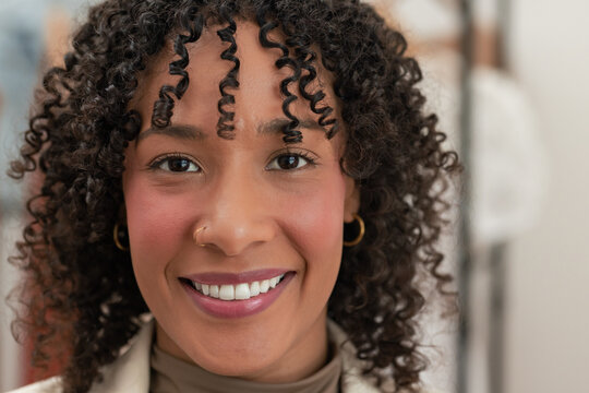 Smiling African American woman wearing beige blazer with gold hoop earrings and nose ring in studio