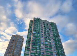 Fototapeta premium Against the background of a blue sky with clouds, there is a modern building with many windows and balconies. I am looking at the facade of a new building.