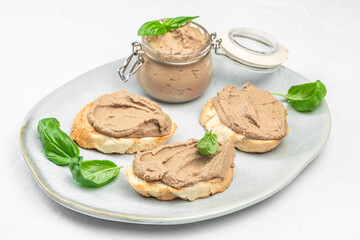 Creamy homemade liver pate in a glass jar with fresh basil, served on toasted bread slices as an elegant appetizer, gourmet spread ideal for menus, culinary blogs and food branding