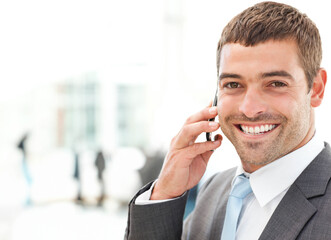 Mid-adult man in gray suit with blue tie talking on smartphone smiling in lobby, copy space