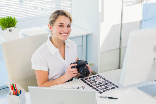 Female photographer wearing white blouse holding DSLR camera, reviewing contact sheet at desk