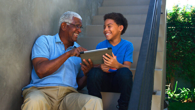 Grandfather With Grandson Sitting On Steps Outdoors At Home Using Digital Tablet - Powered by Adobe