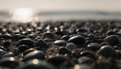 Close-up of smooth dark pebbles on a beach with a bright sun reflection on the water in the background.