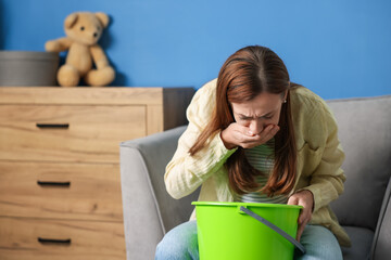Pregnant woman with bucket suffering from nausea in armchair at home. Space for text © New Africa