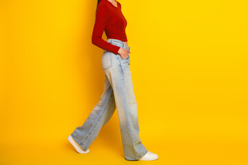 Naklejka premium Young woman in red top and wide light jeans walking against bright yellow background showcasing casual fashion style and confident relaxed lifestyle for lively streetwear image