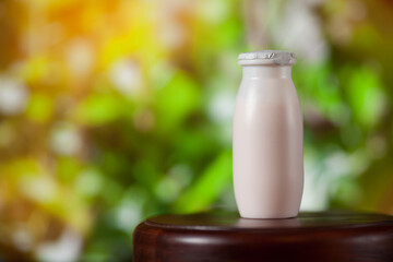 Natural liquid yogurt with probiotics in small plastic bottle on wooden table on background of green trees on a sunny day. Healthy, balanced diet food, healthy breakfast, dairy products.