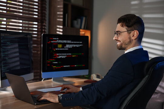 Programmer in glasses working on laptop at table in office