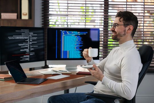 Smiling programmer in glasses with cup of hot drink at workplace