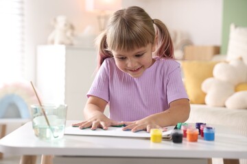 Cute little girl drawing with palms at white table indoors