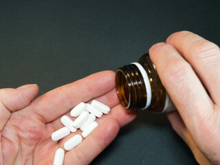 Hand Pouring White Pills from Bottle - Close-up of hands pouring white rectangular pills from a brown medicine bottle. Ideal for health, wellness, daily medication, and pharmacy themes.