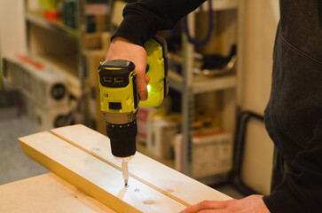 Man driving a screw into a wooden beam with a cordless drill driver in a workshop