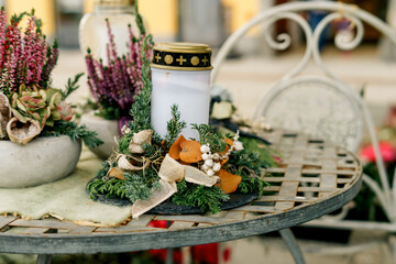 A decorative memorial candle surrounded by autumn leaves, evergreens, and rustic accents displayed on a vintage metal table outdoors