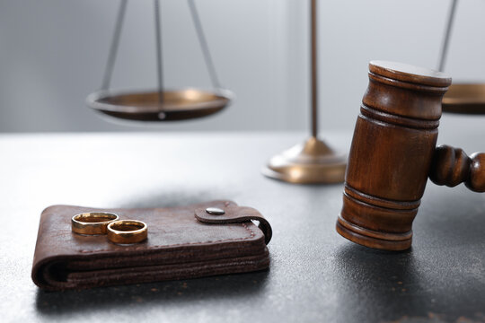 Alimony. Wallet, wedding rings, scales and gavel on dark table, closeup