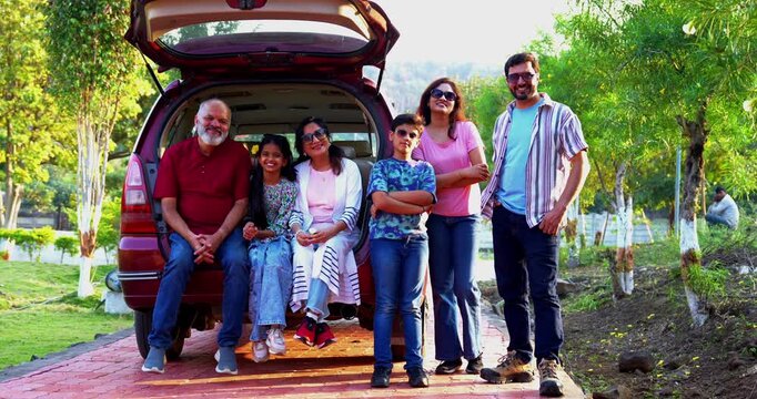 Indian family sitting in car dicky outdoors ready to go for picnic enjoying fun moments, grandparents, parents, and kids relaxing together, sharing laughter and bonding during a joyful outdoor break