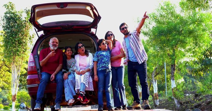 Indian family sitting in car dicky outdoors ready to go for picnic enjoying fun moments, grandparents, parents, and kids relaxing together, sharing laughter and bonding during a joyful outdoor break