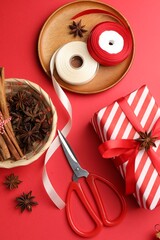 Festive packaging. Gift box, ribbon, scissors, wrapping paper and Christmas decor on red background, flat lay