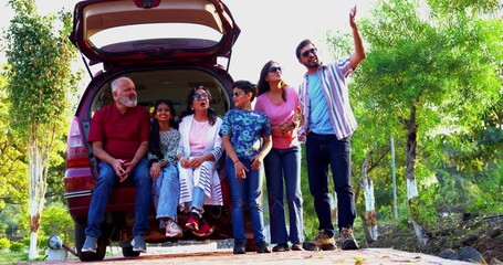 Indian family sitting in car dicky outdoors ready to go for picnic enjoying fun moments, grandparents, parents, and kids relaxing together, sharing laughter and bonding during a joyful outdoor break
